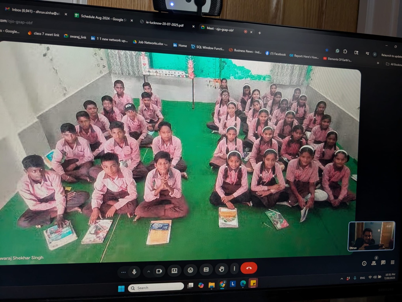 A classroom of students in pink uniforms sitting on the floor with their notebooks during a virtual session