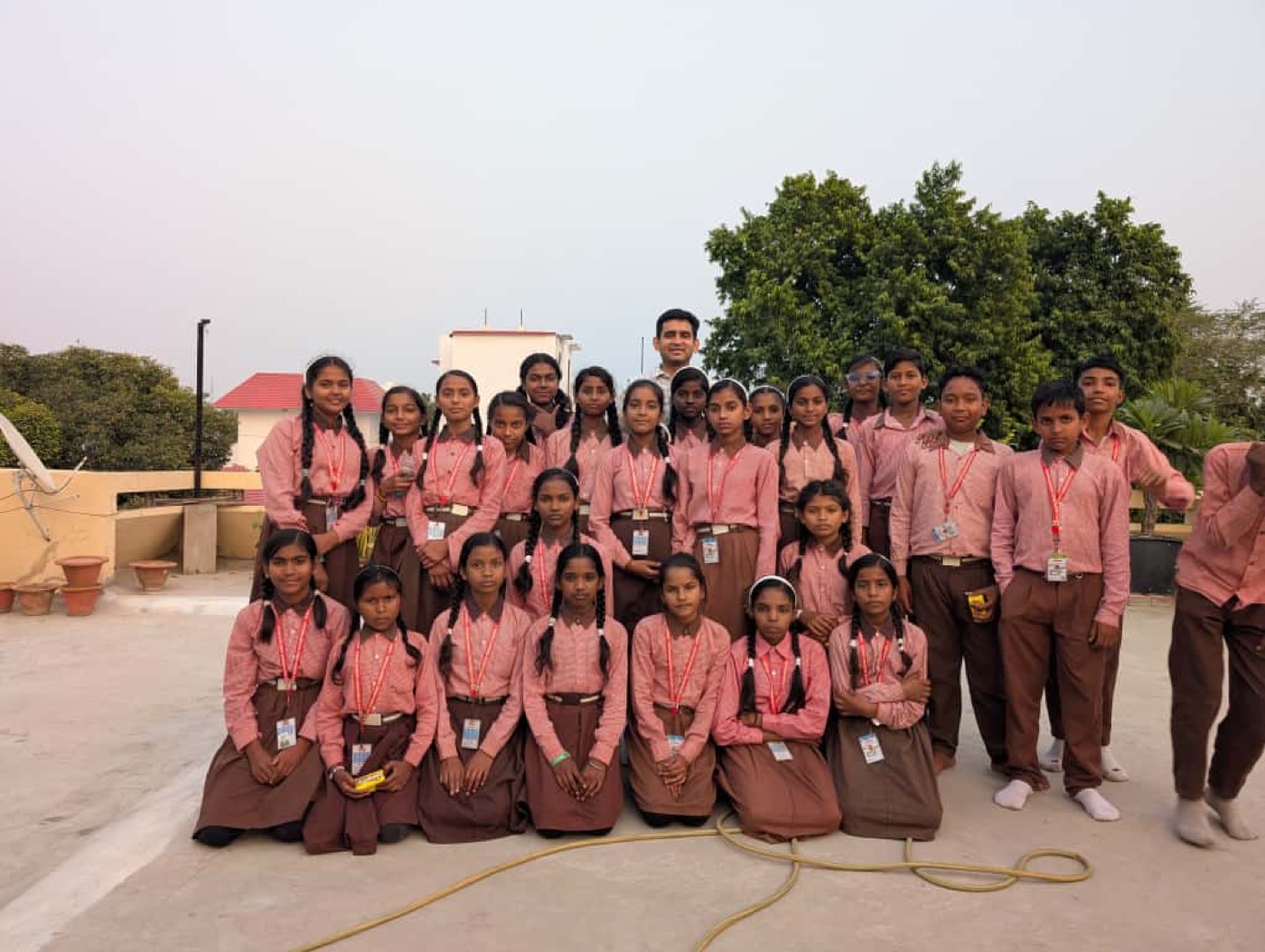 A large group of students in pink uniforms posing together on a rooftop